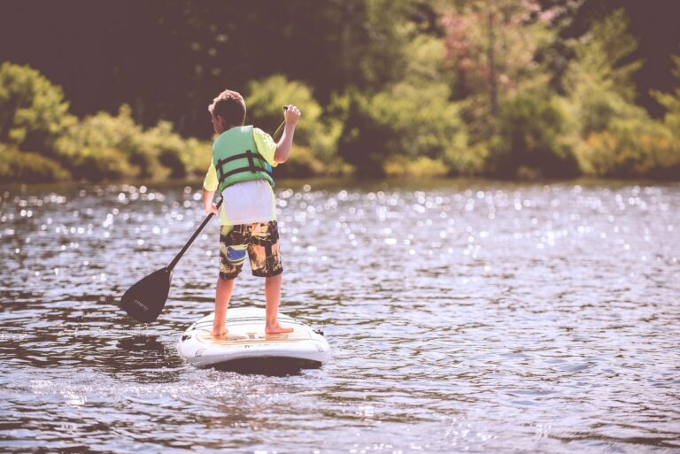 Little boy paddle boarding down a river on a bright, sunny day.