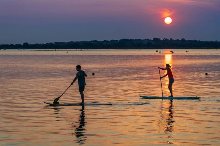 Two people paddle boarding on a calm lake at night while the sun is setting.