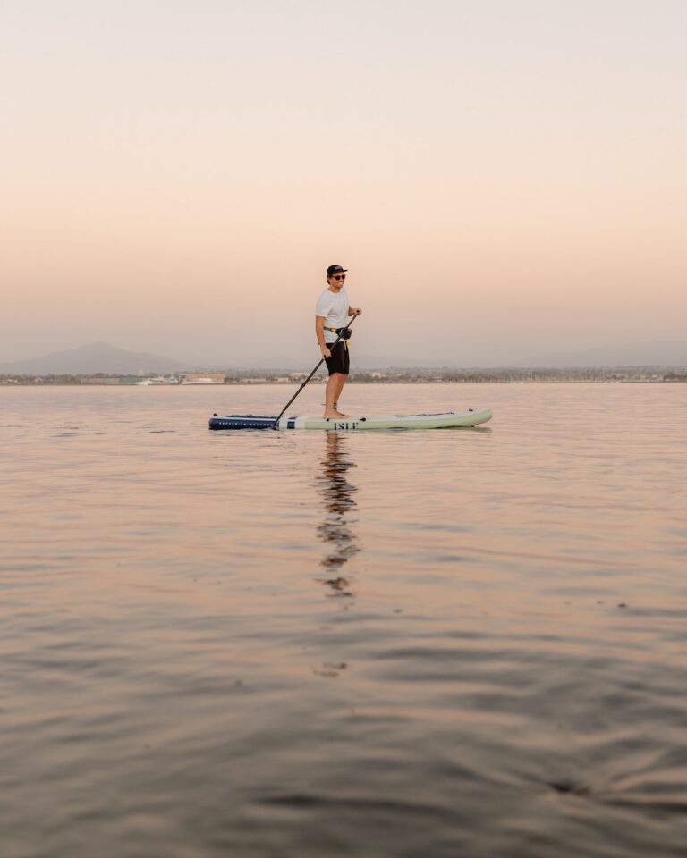 Man paddle boarding on a calm lake during a sunset.